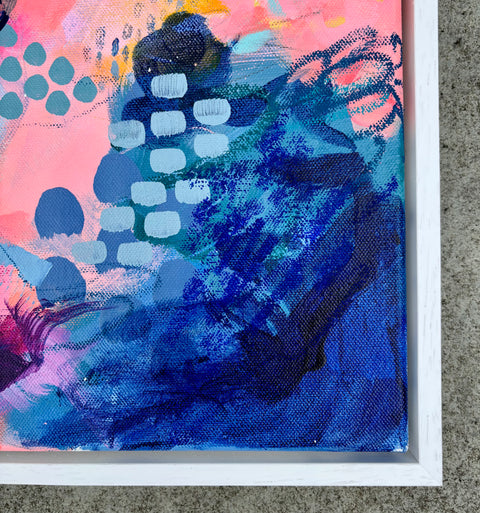 Abstract canvas painting in a white frame, featuring vibrant blue and pink brushstrokes with white painted dots and textured paint details.